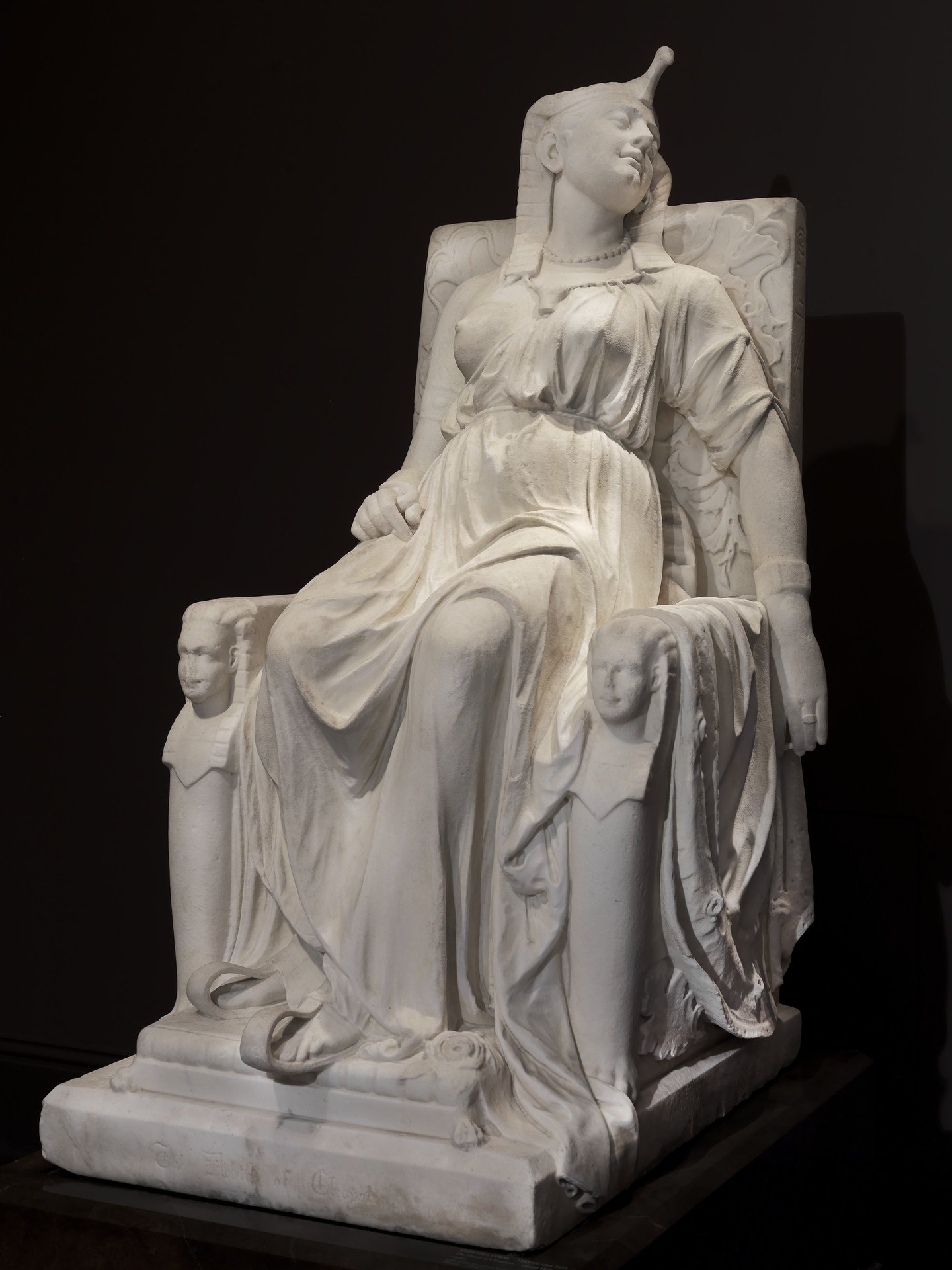 Museum view 1: a marble figure of Cleopatra slumps on a throne with carved sphinx heads on its arms; her head tilts to one side.
