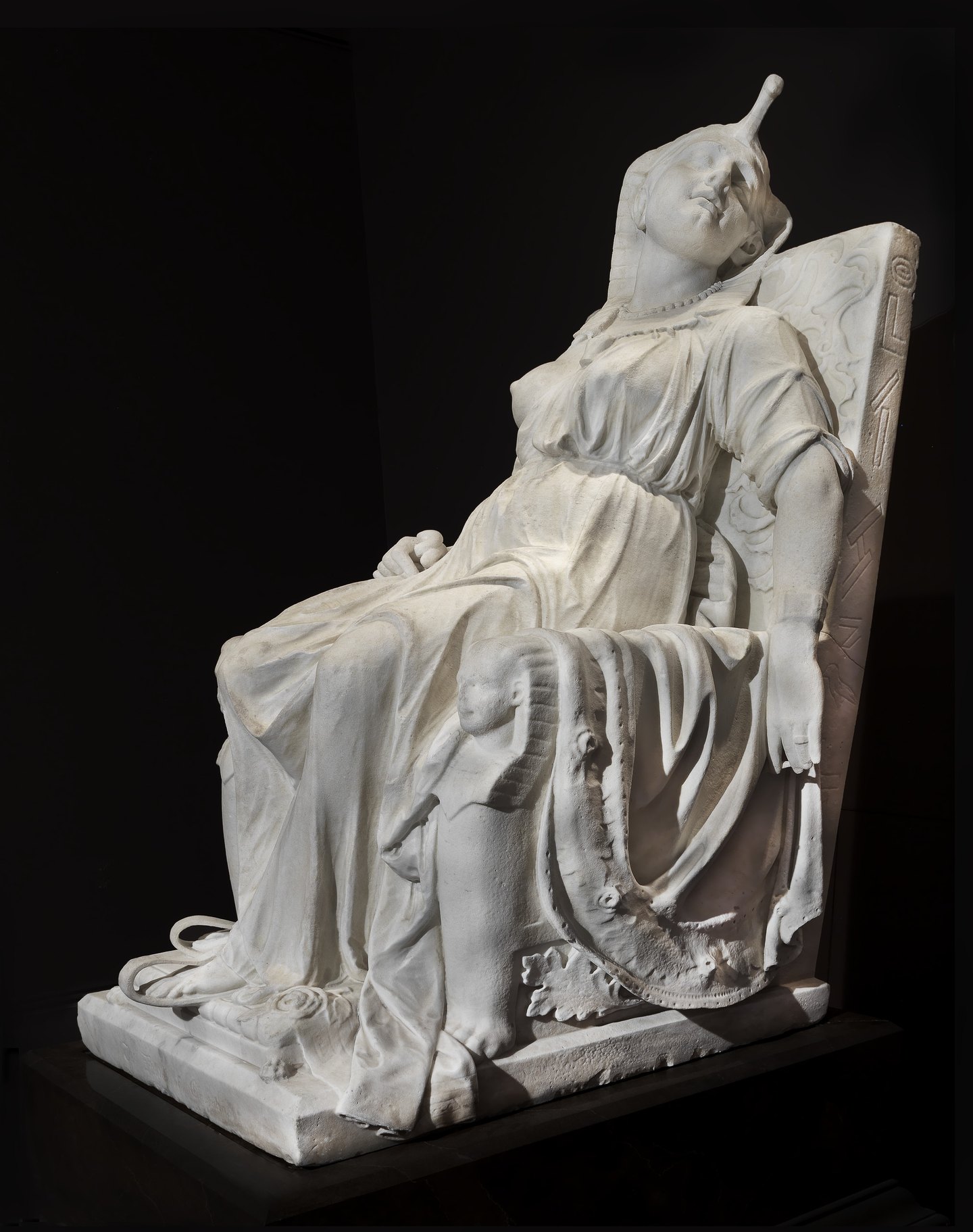 Museum view 2: the same sculpture from a different angle, showing the throne's side and the fall of drapery across the figure.