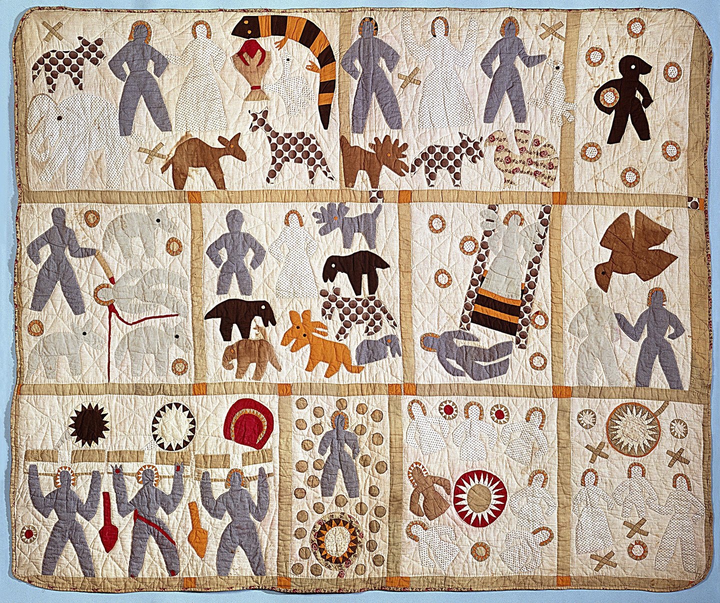A rectangular quilt with eleven bordered panels of appliquéd human and animal figures, stars and other shapes in contrasting fabrics.